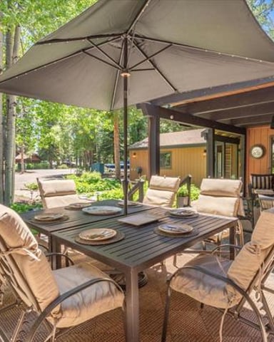 Shaded patio dining area with table, chairs, and umbrella adjacent to wood cabin