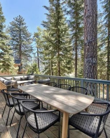 Spacious deck with dining table, chairs, and lounge seating surrounded by tall pine trees