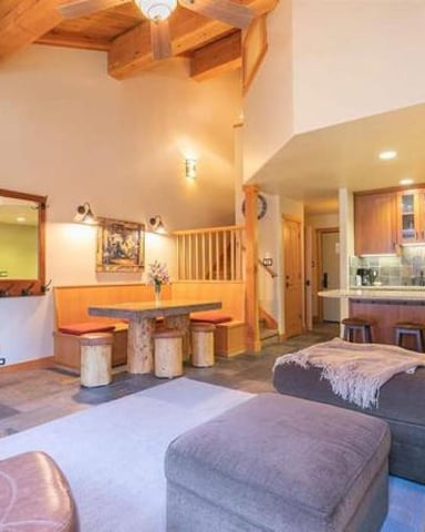 Open-plan loft with stone fireplace, exposed wood beams, seating area, kitchen, and bedroom loft above