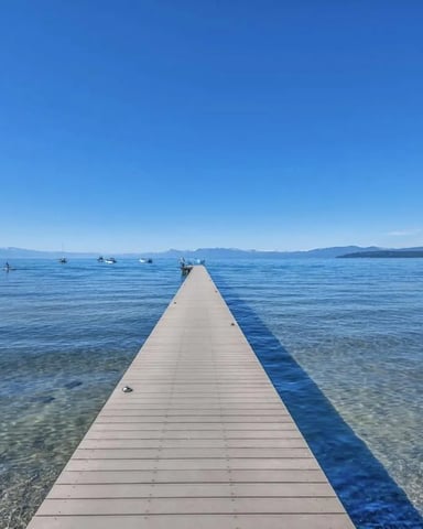Long wooden dock extending into clear blue lake with forested shoreline and mountains in distance