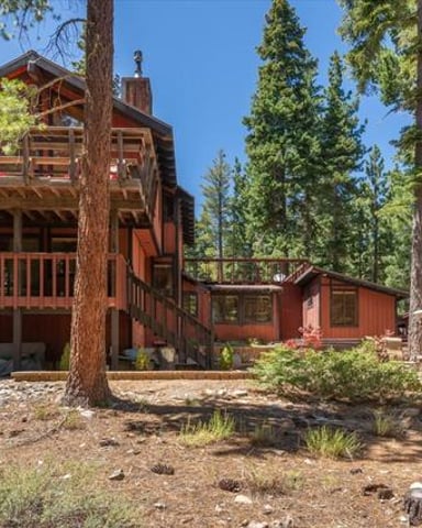 Red wooden cabin with multiple decks surrounded by tall pine trees in a forest clearing