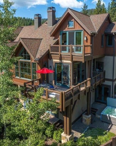 Modern mountain home with wood and stone exterior, red patio umbrella, multi-level decks, surrounded by tall pine trees