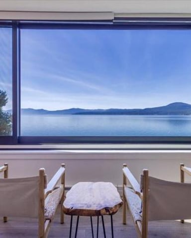 Modern living room with two canvas chairs facing large windows overlooking calm lake and mountains