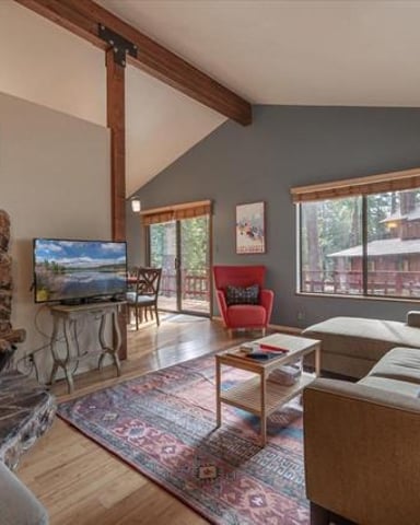 Open-plan living room with fireplace, brown sofa, red armchair, and large windows overlooking deck