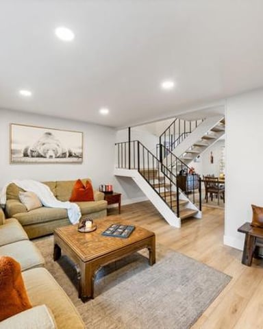 Open-plan living room with beige sectional sofa, wooden coffee table, and decorative skis on wall, stairs visible in background