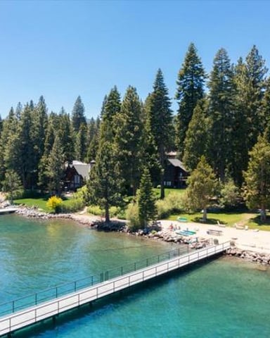 Lakeside homes nestled among tall evergreen trees with a wooden dock extending into clear turquoise water