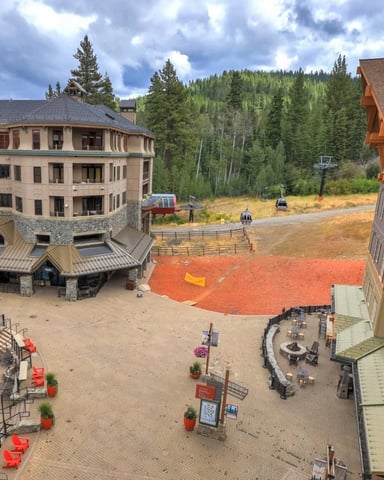 Resort courtyard with large stone and wood lodges, central plaza with fire pit, red sports court, and forested mountains beyond