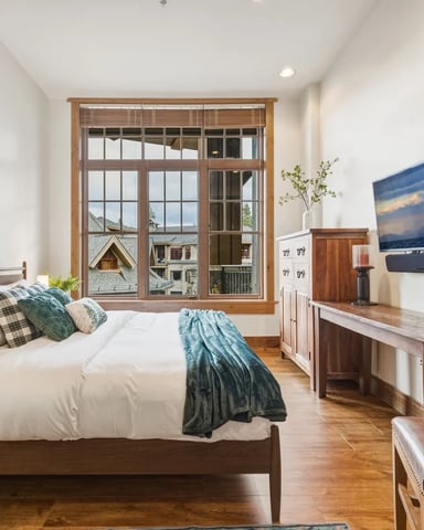 Bedroom with wood bed, white bedding, large windows with mountain views, TV on wall, and hardwood floors