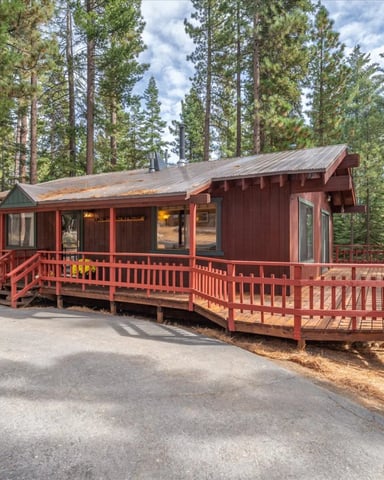 Red cabin with wraparound deck surrounded by tall pine trees in forest setting