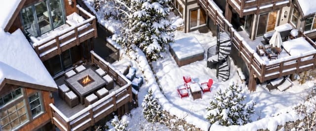 Aerial view of three snow-covered mountain homes with decks, fire pit, and red chairs nestled among evergreen and aspen trees
