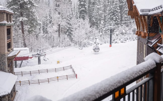 Snowy ski resort with chairlifts, wooden lodge buildings, and snow-covered evergreen forest in background